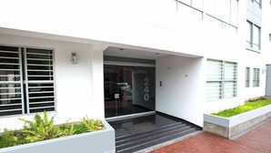 Ein moderner Gebäudeeingang mit Glastür, der Hausnummer '240' an der Wand und einem Pflasterweg, der zum Eingang führt.