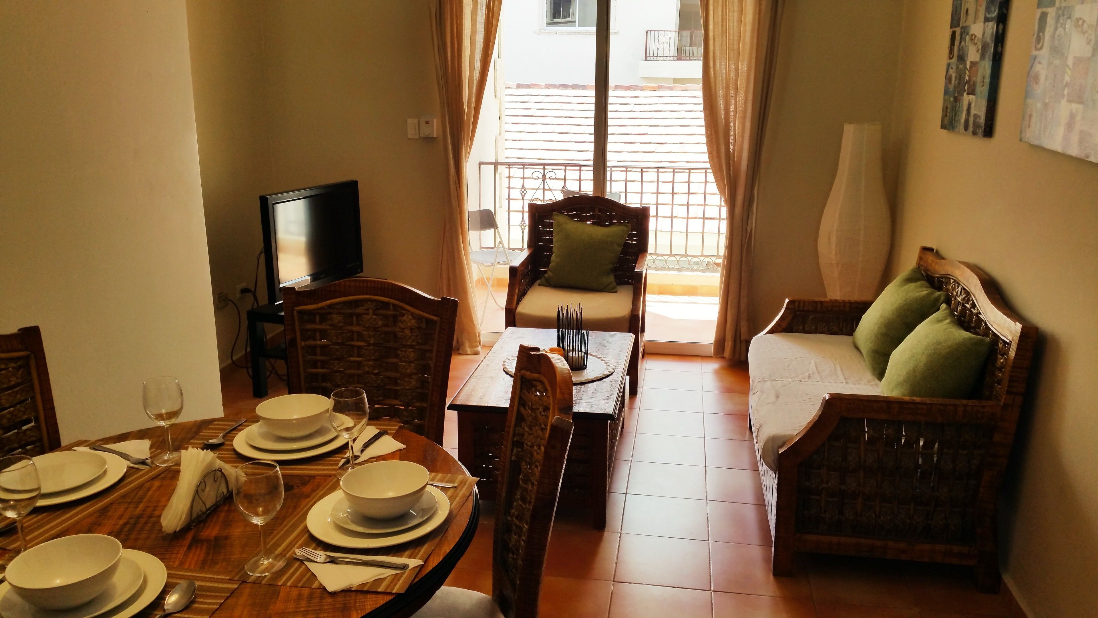 A dining area with a table set for four, a television, and a sofa with cushions.