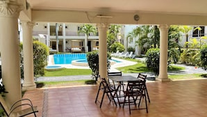 Un patio couvert avec une piscine, des sièges d’extérieur et une vue sur un immeuble à plusieurs étages.
