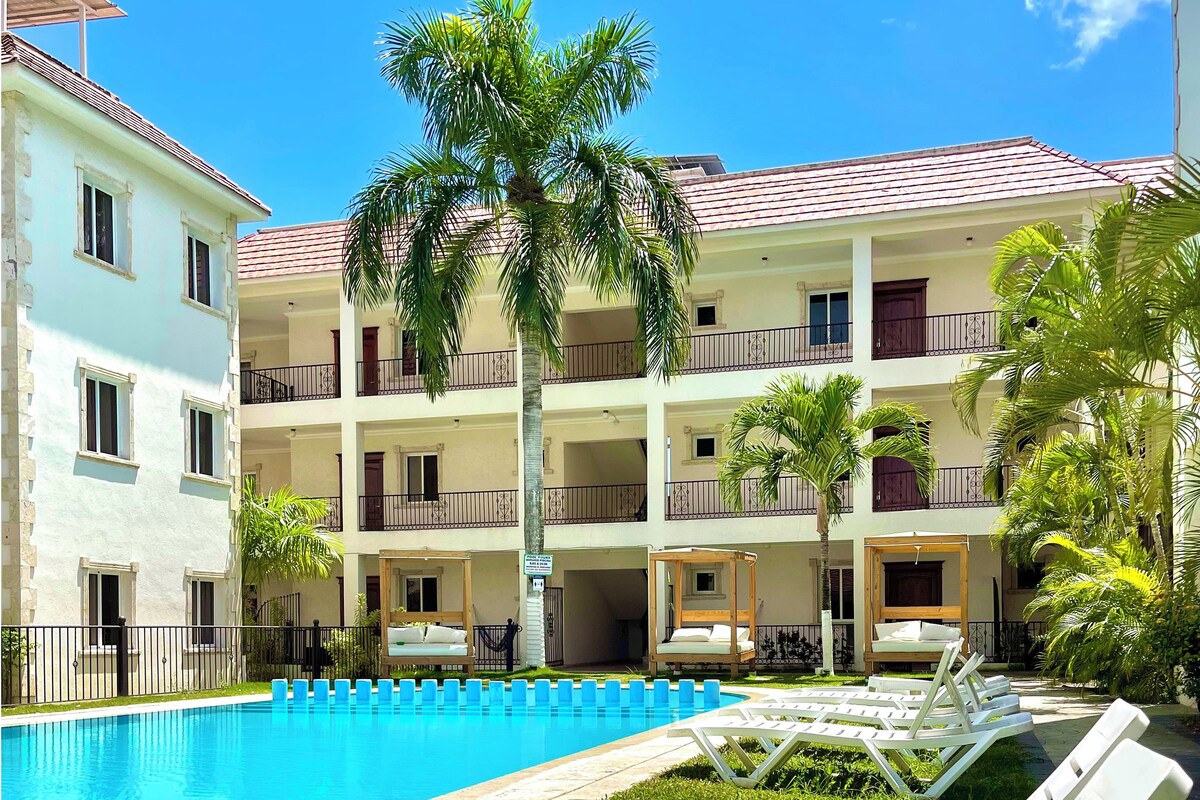 A hotel with a swimming pool, lounge chairs, and palm trees.