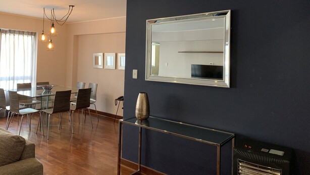Una sala de estar moderna con una mesa de comedor de vidrio, asientos cómodos, un espejo grande y una radio antigua.