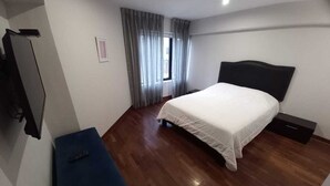 Una habitación de hotel con cama, escritorio, armario y ventana con cortinas.