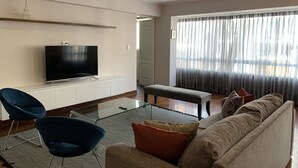 Una sala de estar moderna con una televisión de pantalla plana, una mesa de centro de vidrio, un sofá y un banco.