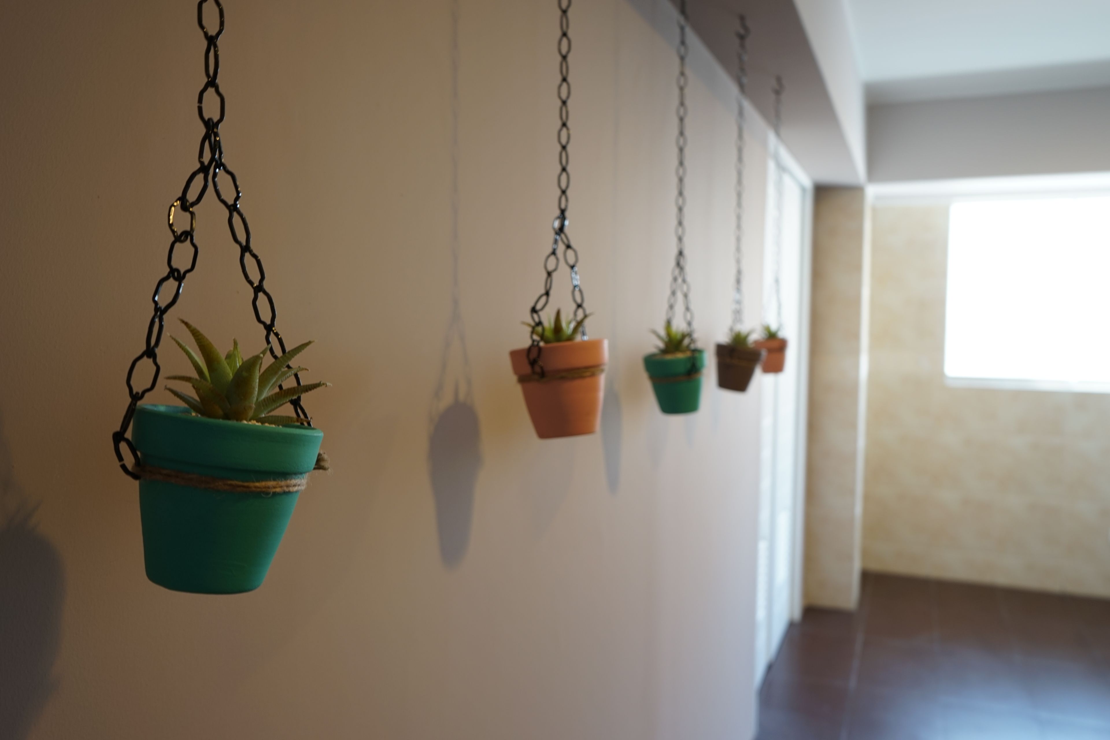 Une série de jardinières suspendues, de différentes tailles et couleurs, accrochées au plafond d’un couloir bien éclairé.