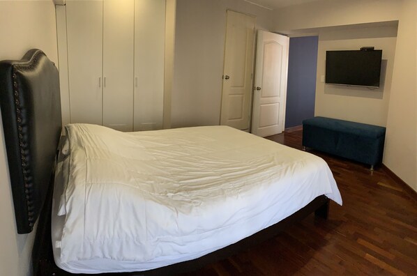 A bedroom with a bed, a wardrobe, a bench, and a TV mounted on the wall.