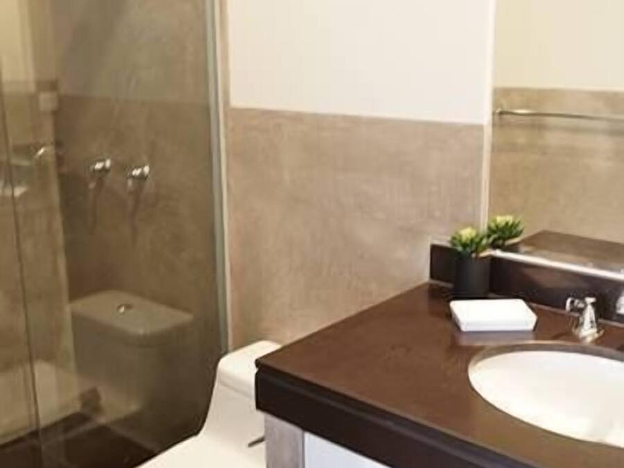 Un baño con cabina de ducha de vidrio, inodoro blanco y encimera marrón oscuro con lavabo y armarios.