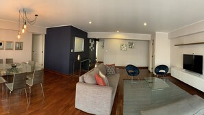 Una sala de estar moderna con una mesa de comedor de vidrio, un sofá gris y un televisor montado en la pared.