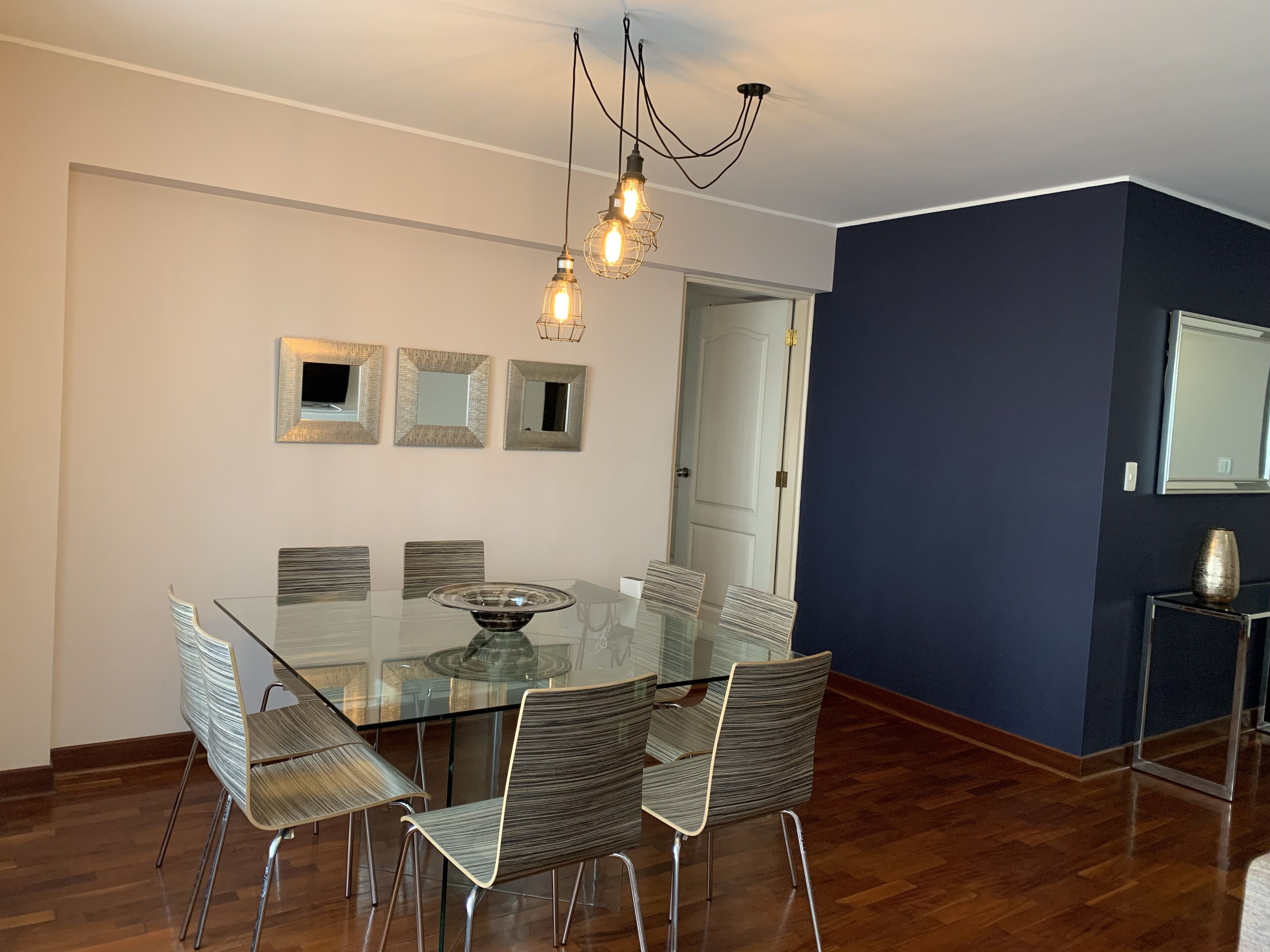 A dining area with a glass table, six chairs, and a chandelier.