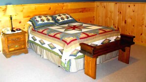 A bedroom with a wooden headboard, a bed with a quilt, a nightstand, and a wooden bench. - Heritage Inn (Richfield Springs)