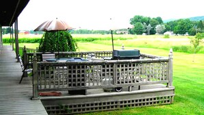 A covered outdoor deck with a grill and umbrella, surrounded by a wooden fence and a well-maintained lawn. - Heritage Inn (Richfield Springs)