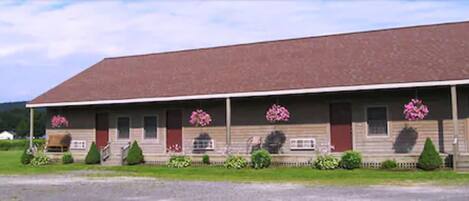 A two-story building with a red roof and a porch with potted plants.