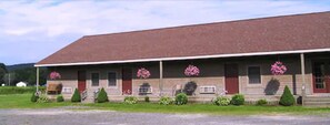 A two-story building with a red roof and a porch with potted plants.