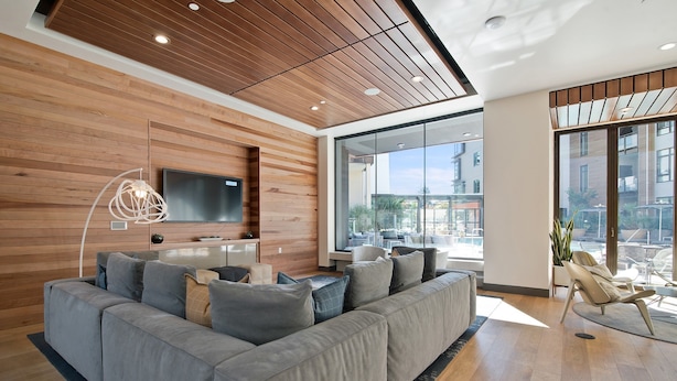A modern living room with a grey sectional sofa, wooden ceiling, large windows, and a flat-screen TV. - Global Luxury Suites at Mountain View (Mountain View)