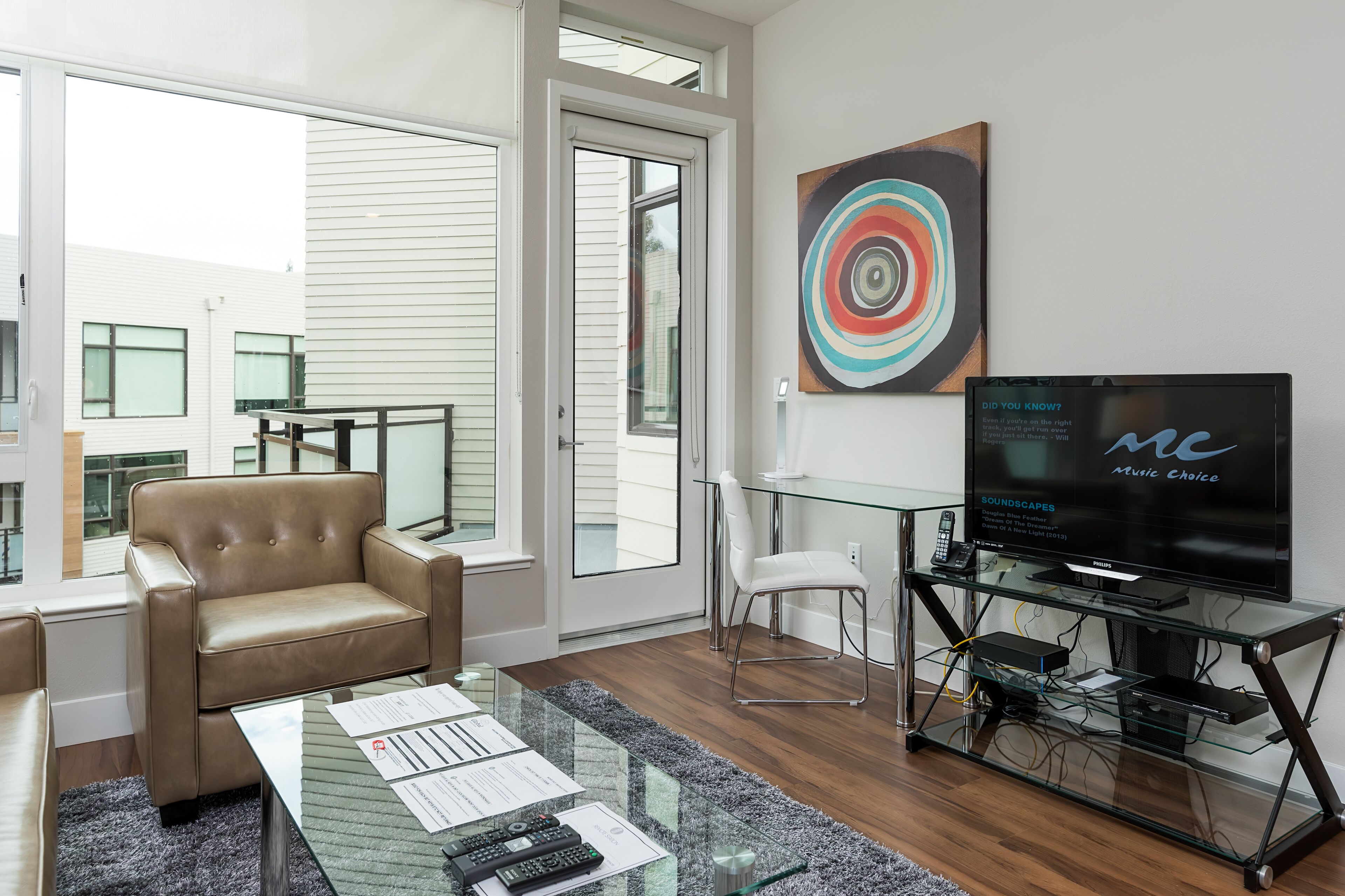 Uma sala de estar moderna com uma mesa de centro de vidro, poltrona de couro e uma TV de tela plana em um suporte de vidro.