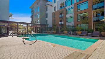 A modern hotel with a rooftop pool, outdoor seating, and a clear blue sky.