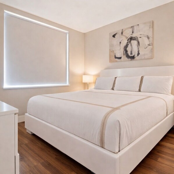 Un dormitorio con una cama grande, una mesita de noche, una lámpara y una ventana con persianas.