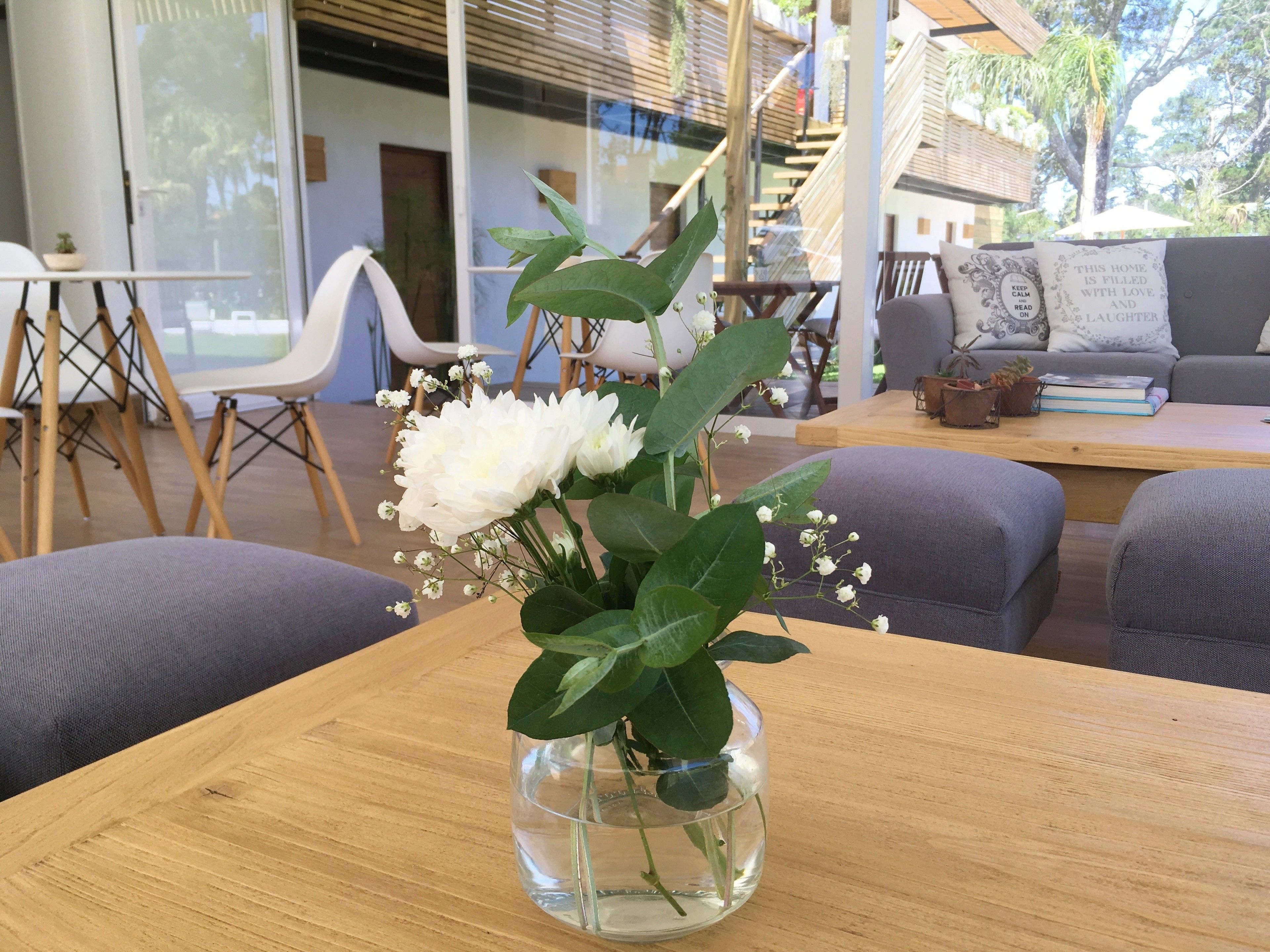 Une table en bois sur laquelle est posé un vase en verre transparent contenant des fleurs blanches et des feuilles vertes.