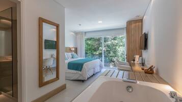 Une chambre d’hôtel moderne dotée d’un grand lit, d’un coin salon avec vue, d’une baignoire et d’un balcon offrant une vue sur la verdure environnante.