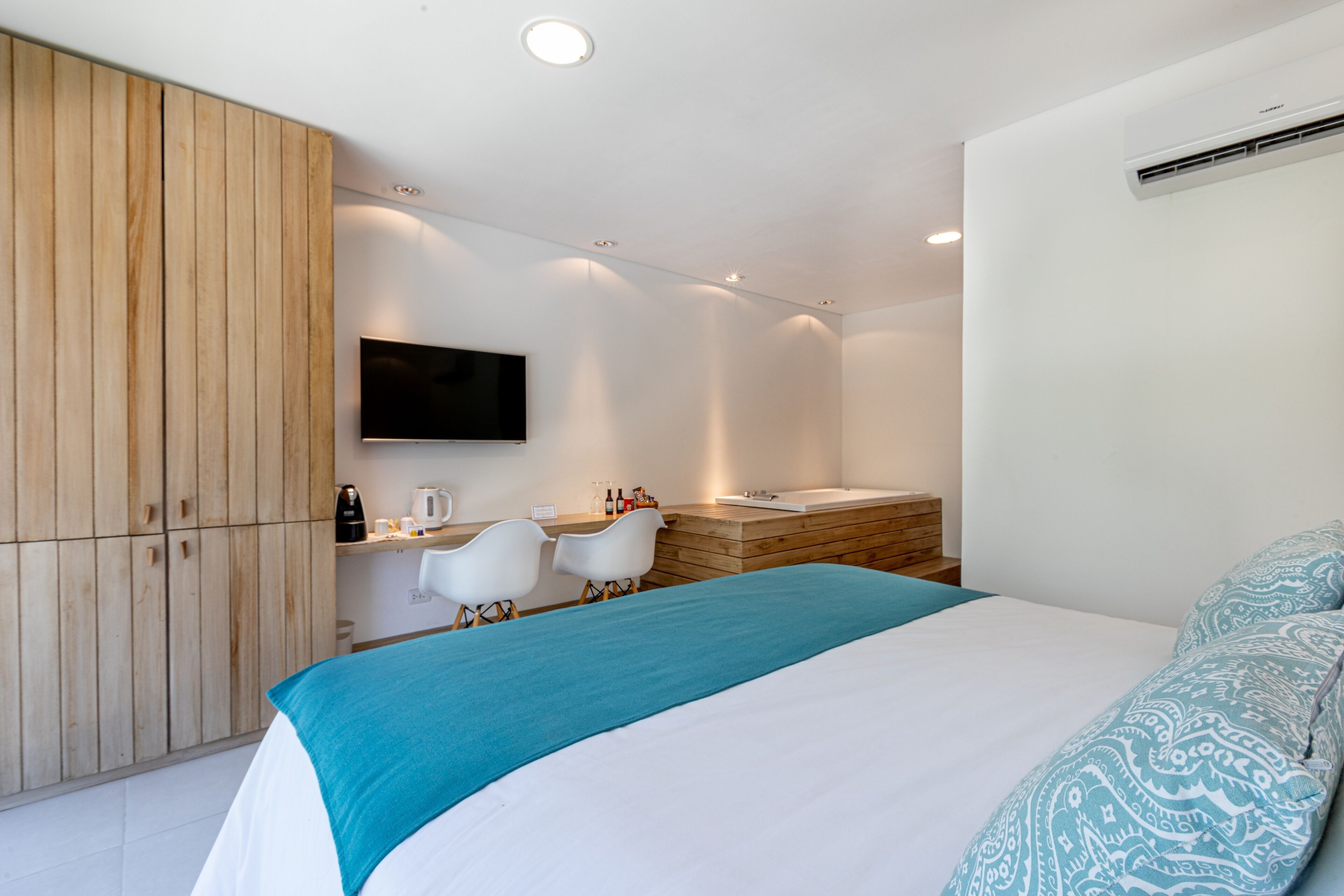 Una habitación de hotel moderna con una cama grande, un armario de madera, un televisor de pantalla plana, un baño con bañera y una pequeña zona de estar.
