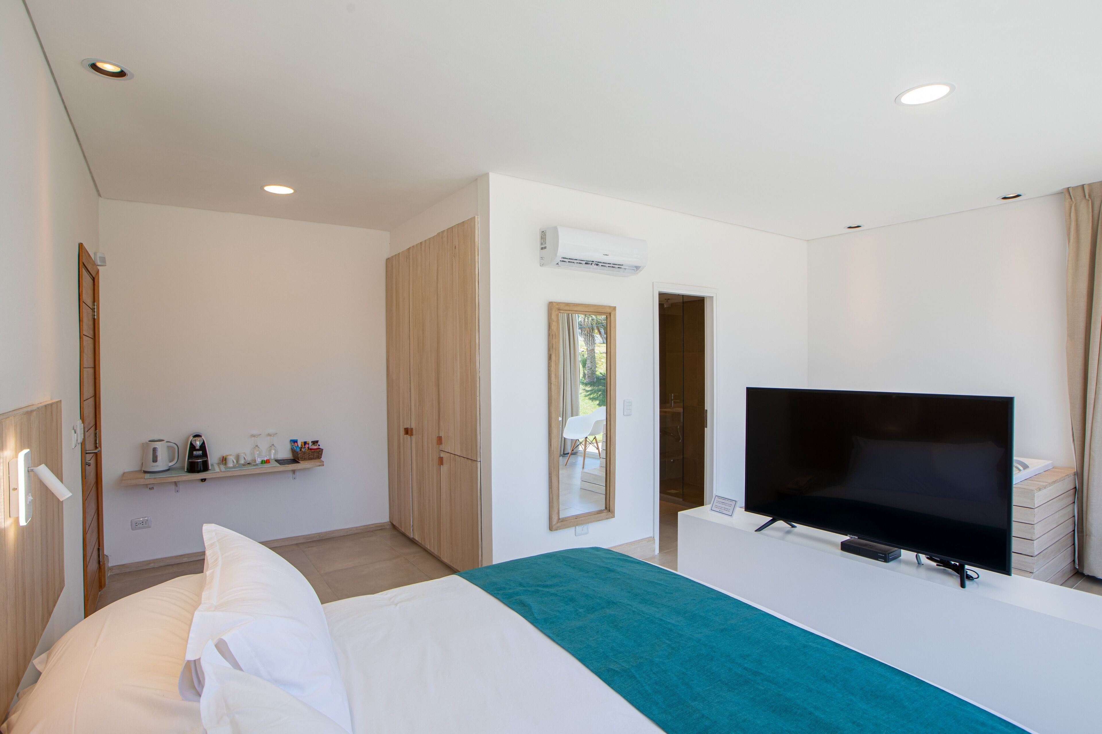 Una habitación de hotel moderna con una cama, un televisor, un espejo y un estante con artículos de aseo.