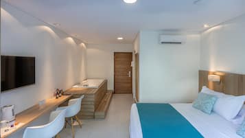 Une chambre d’hôtel comprenant un lit, un bureau avec des chaises, un banc en bois, une télévision et un appareil de climatisation.
