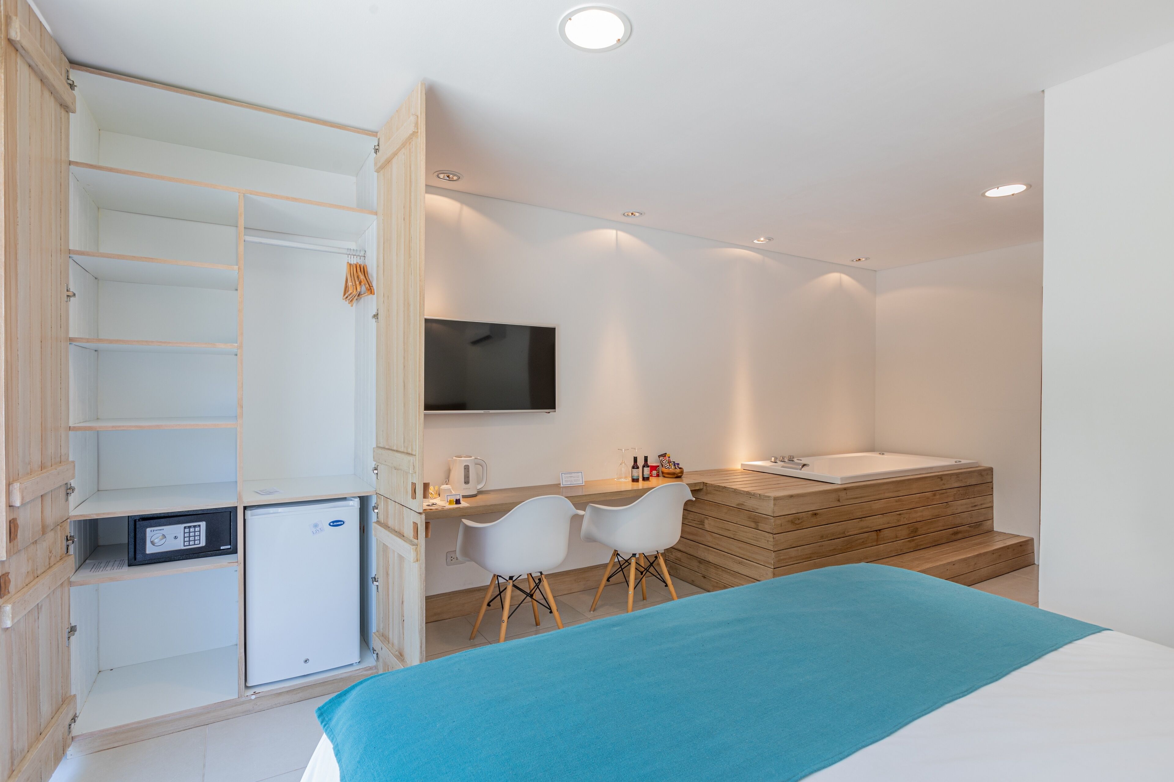 Une chambre d’hôtel moderne équipée d’un lit, d’un bureau, d’une chaise, d’une télévision, d’un mini-réfrigérateur et d’une salle de bain avec baignoire et douche.
