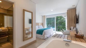 Un dormitorio moderno con una cama grande, un baño con bañera y un balcón con vistas a árboles.