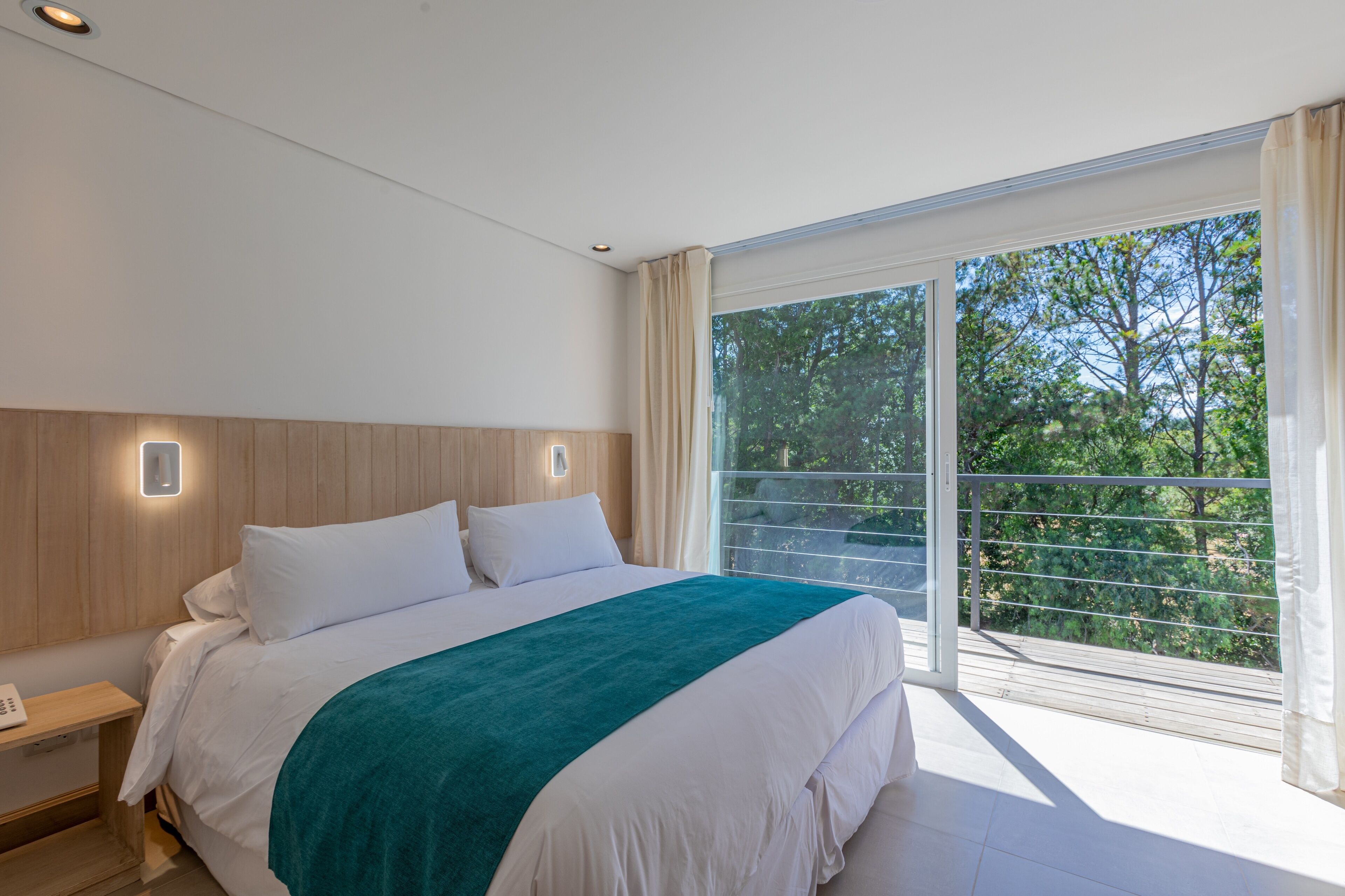 Una camera da letto moderna con un letto grande, una testata in legno, un comodino e vista su del verde da un balcone.