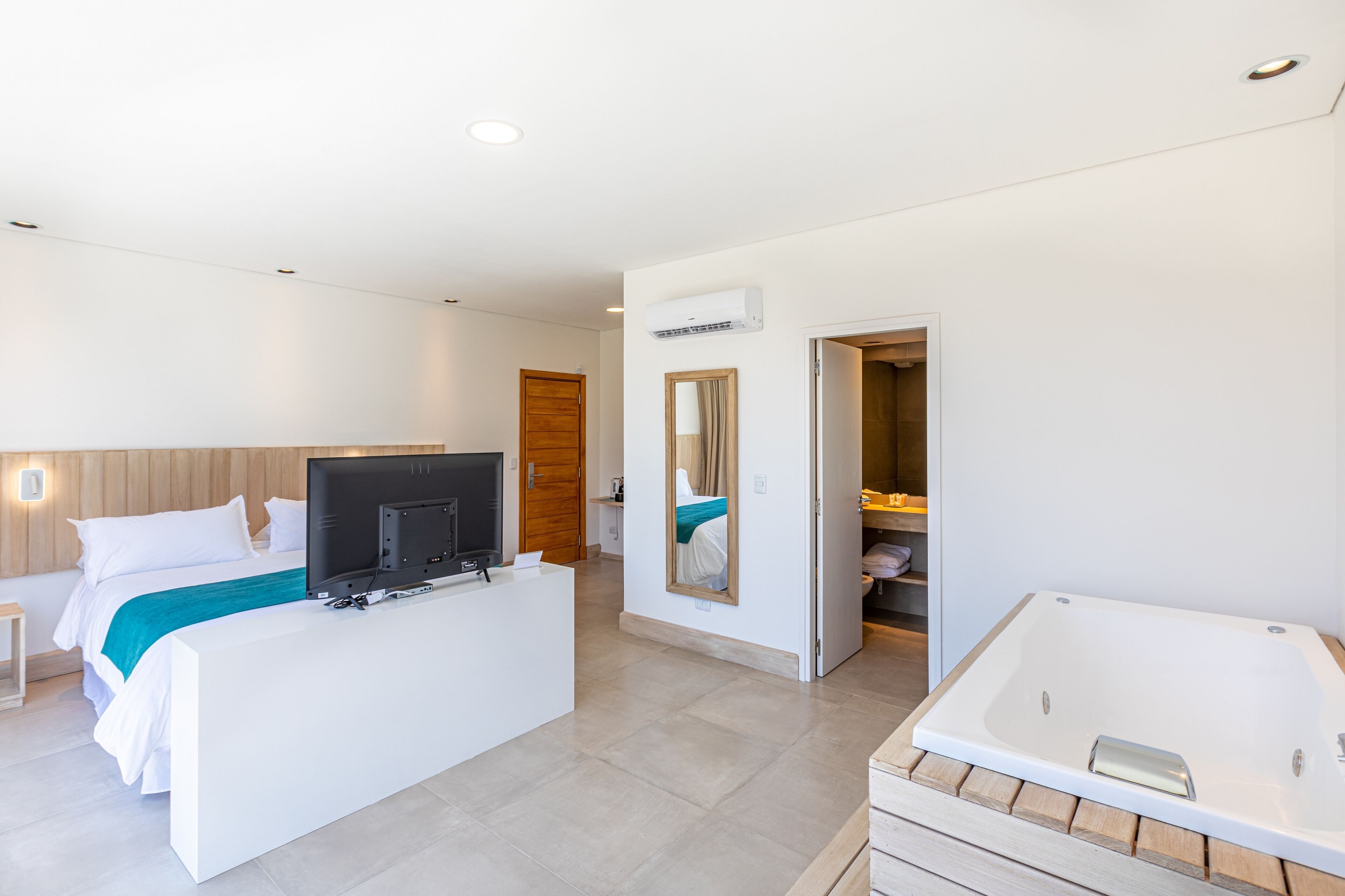Et moderne hotelværelse med seng, skrivebord med tv, et stort badekar og et walk-in closet.