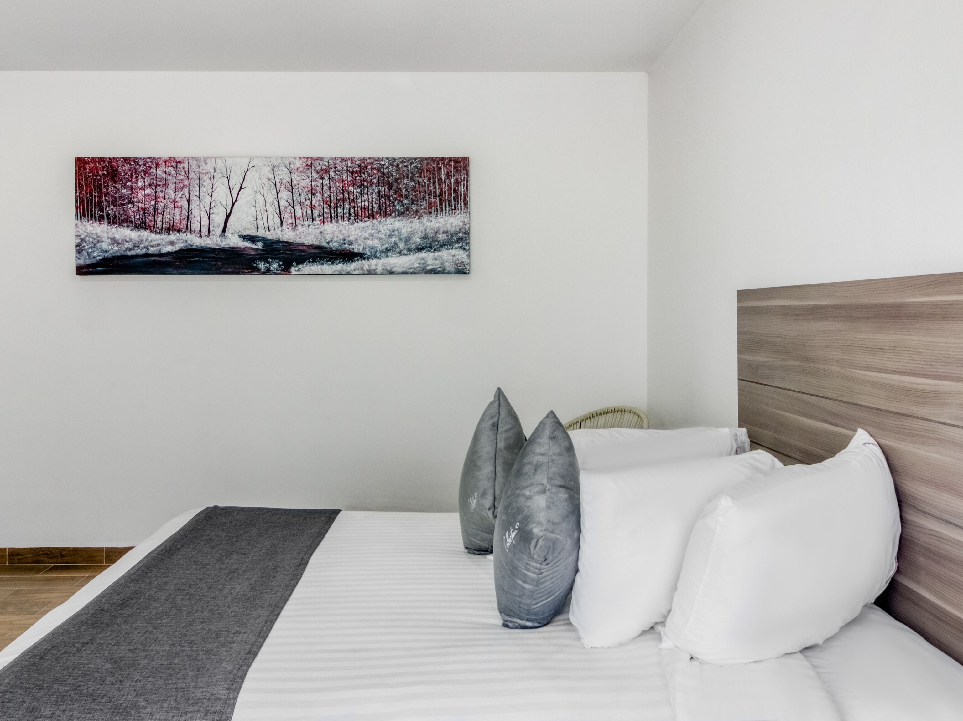 A modern bedroom with a bed, pillows, a blanket, and a painting of a winter landscape on the wall.