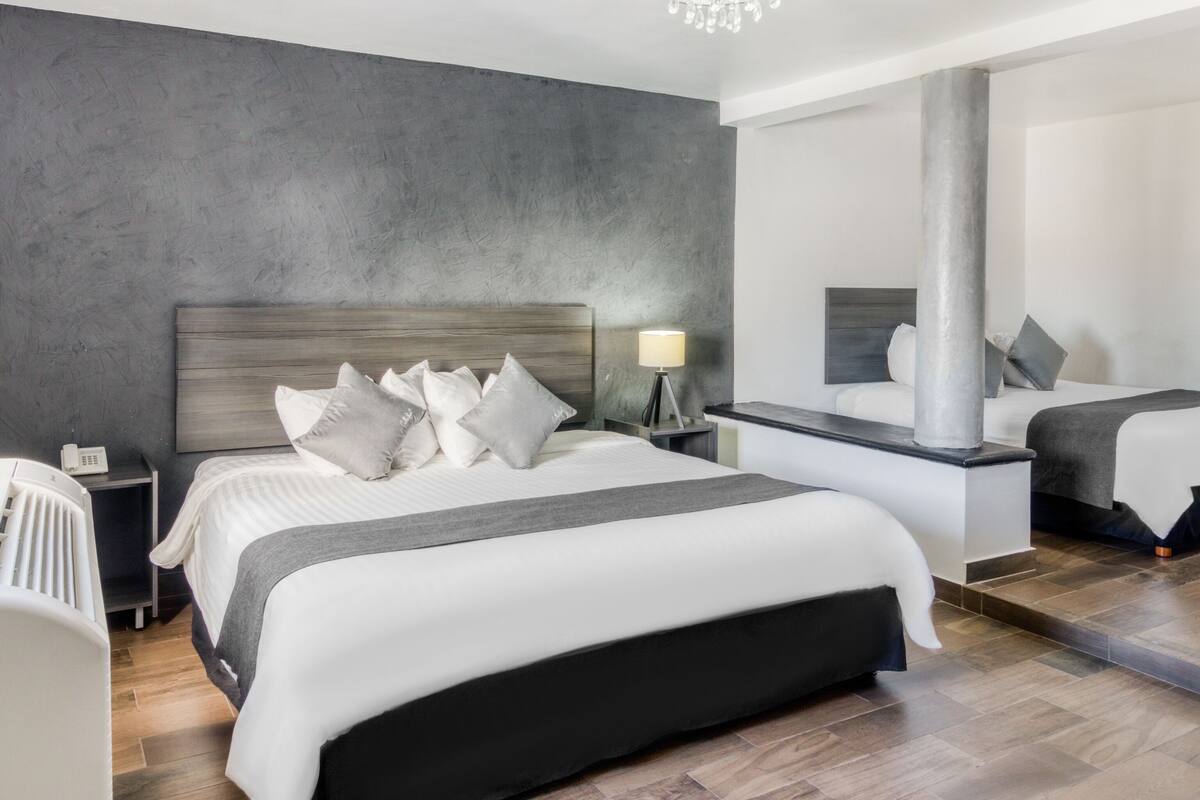 Una habitación de hotel moderna con una cama grande, mesitas de noche, un espejo y una araña.