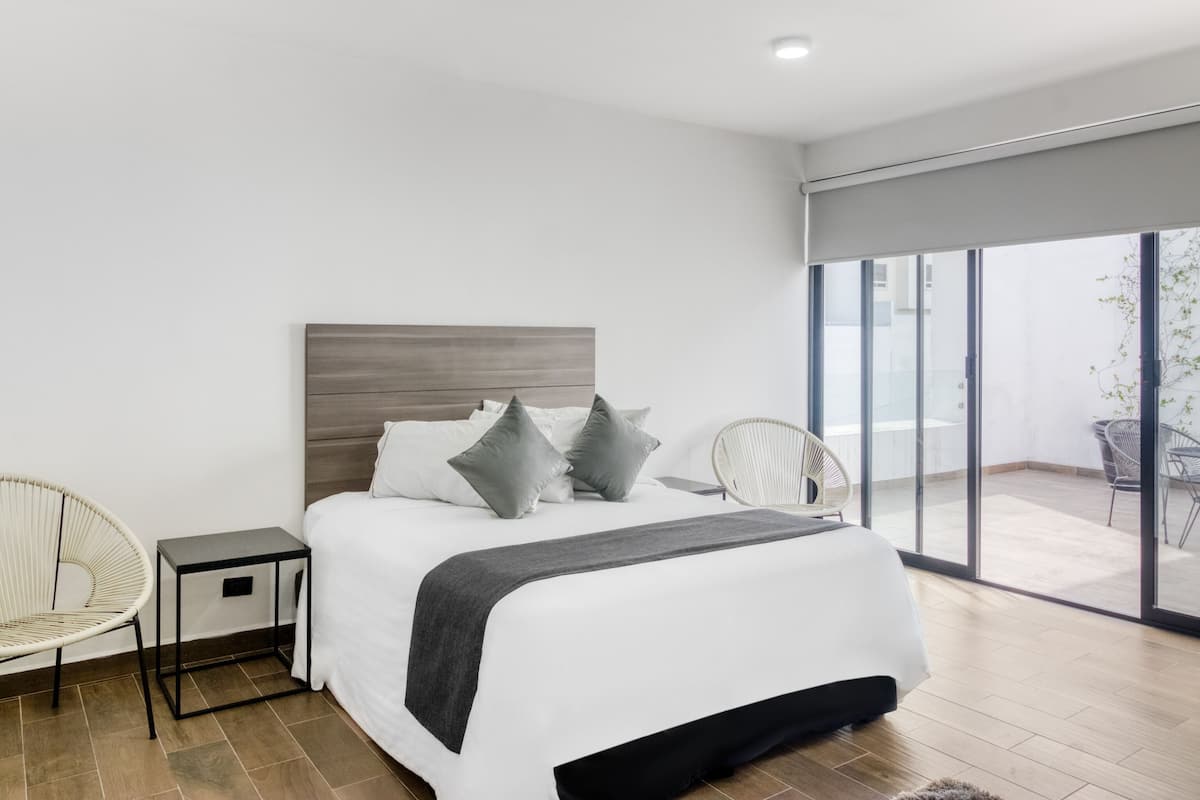 Un dormitorio moderno con una cama grande, una mesita de noche, una silla y vistas a un balcón.