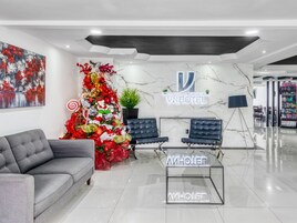 Un moderno vestíbulo de hotel con un mostrador de recepción de mármol, dos sillones de cuero negro, un sofá gris y un gran árbol de Navidad.