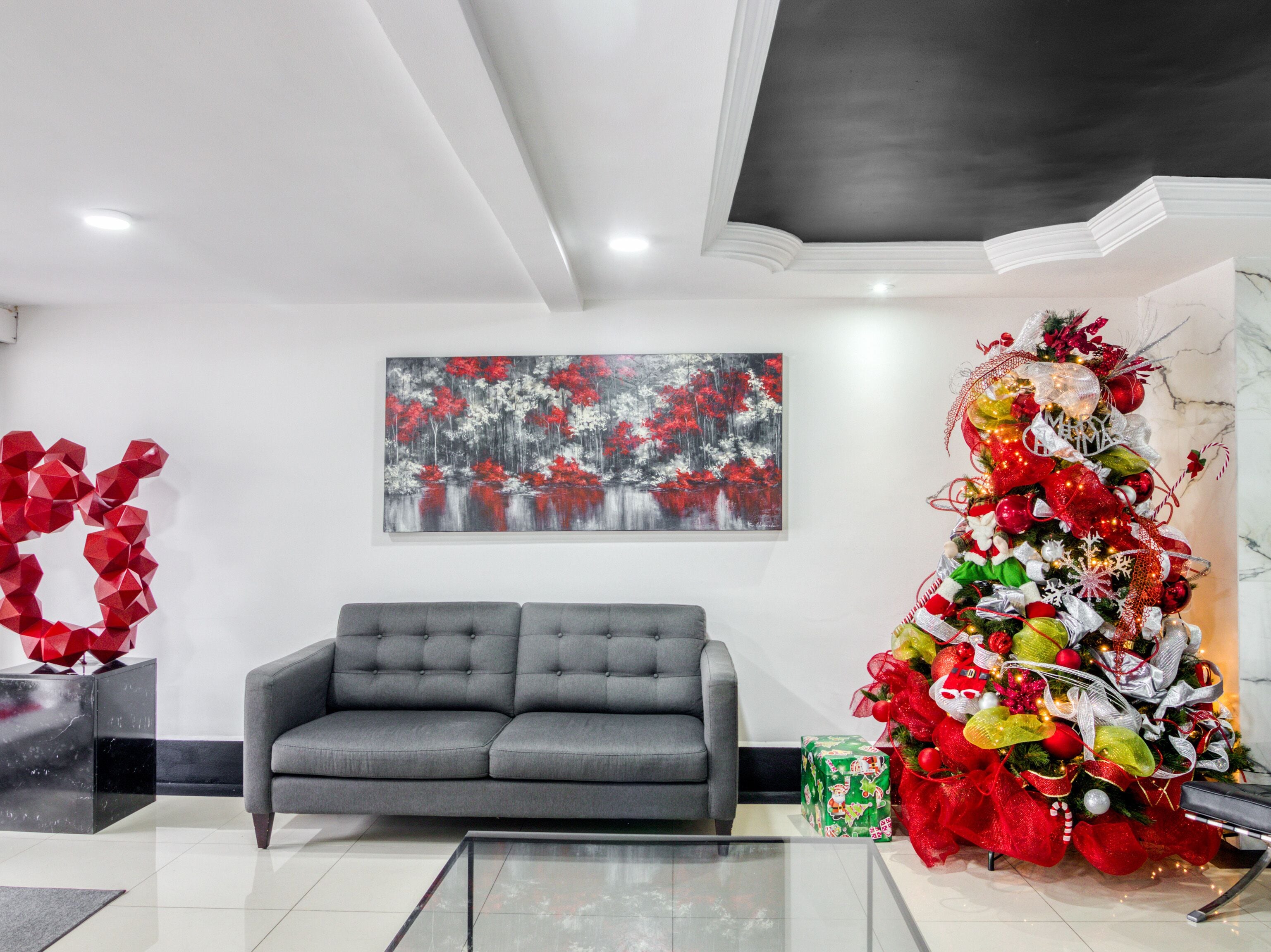 A modern living room with a grey sofa, a large abstract painting, and a decorated Christmas tree.