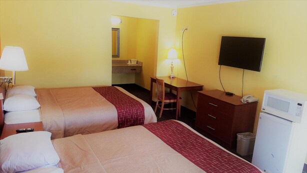 Habitación de hotel con dos camas, un escritorio, una silla, un televisor y un microondas.