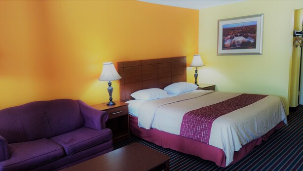A hotel room with a bed, two bedside lamps, a nightstand, a purple armchair, and a small table.