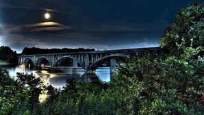 A bridge over a calm river at night with a full moon in the sky.