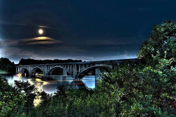 A bridge over a calm river at night with a full moon in the sky.