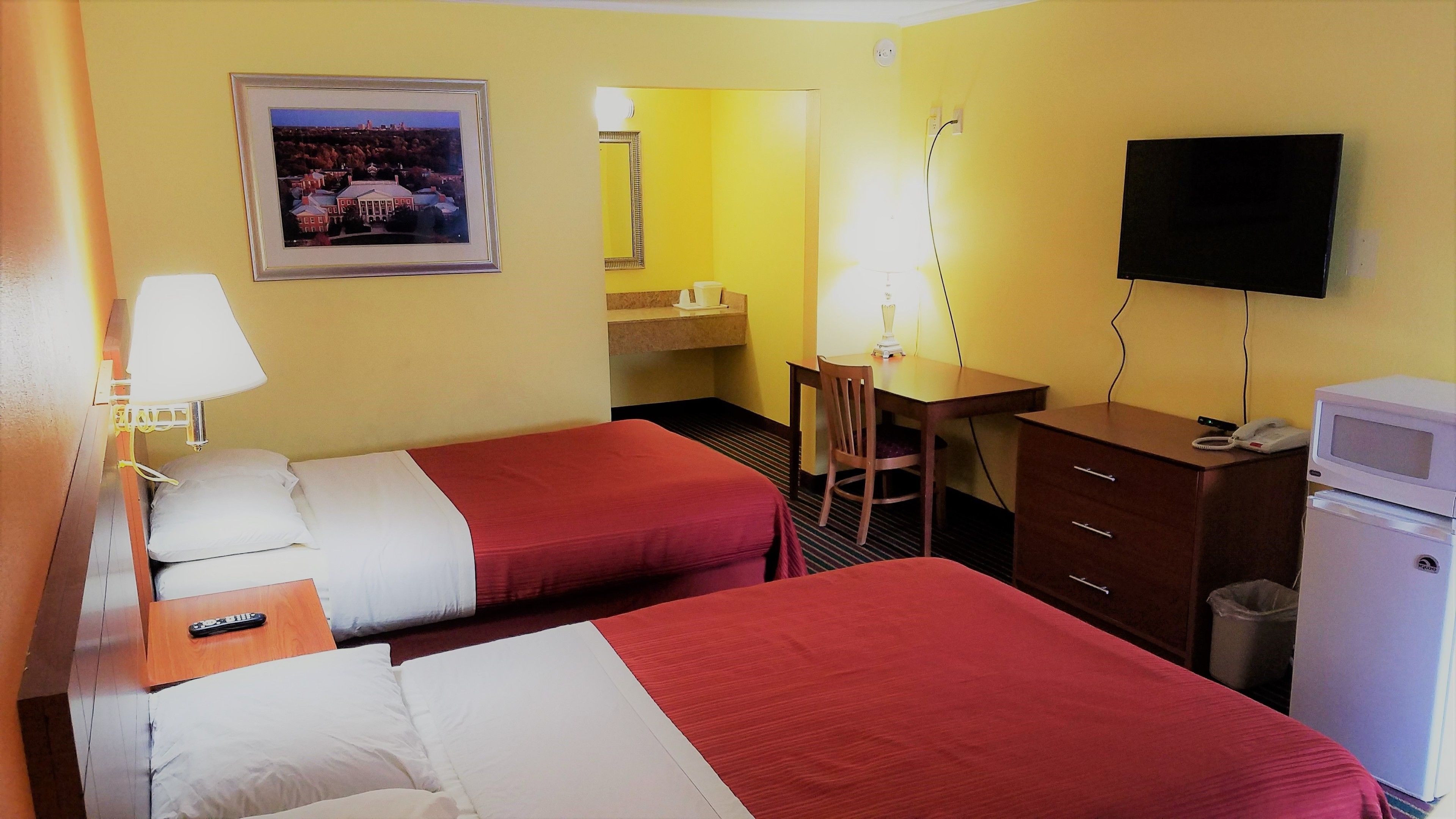Hotelkamer met twee bedden, een bureau, een stoel, een televisie, een magnetron en een prullenbak.