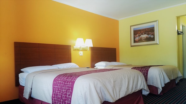 Une chambre d’hôtel avec deux lits, chacun doté d’une tête de lit et d’oreillers, d’une table de chevet, d’une lampe fixée au mur et d’un tableau encadré accroché au mur.