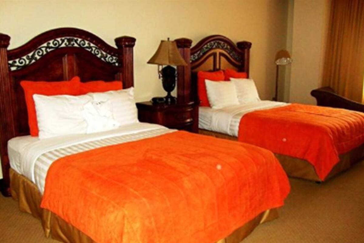 Ein Hotelzimmer mit zwei Betten, jeweils mit einem Holzkopfteil und orangefarbener Bettwäsche.