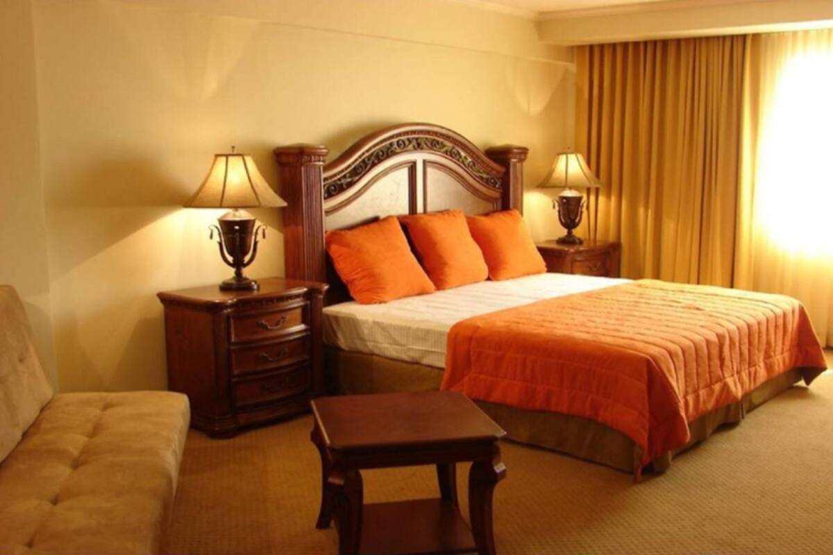 Ein Hotelzimmer mit einem Bett, zwei Nachttischen mit Lampen, einem kleinen Tisch und einem Sofa.