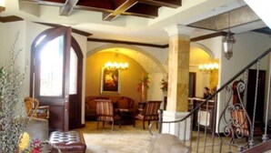 A spacious living area with a high ceiling, a staircase with ornate railings, and a cozy seating arrangement with a fireplace. - Hotel Gran Mediterraneo (San Pedro Sula)