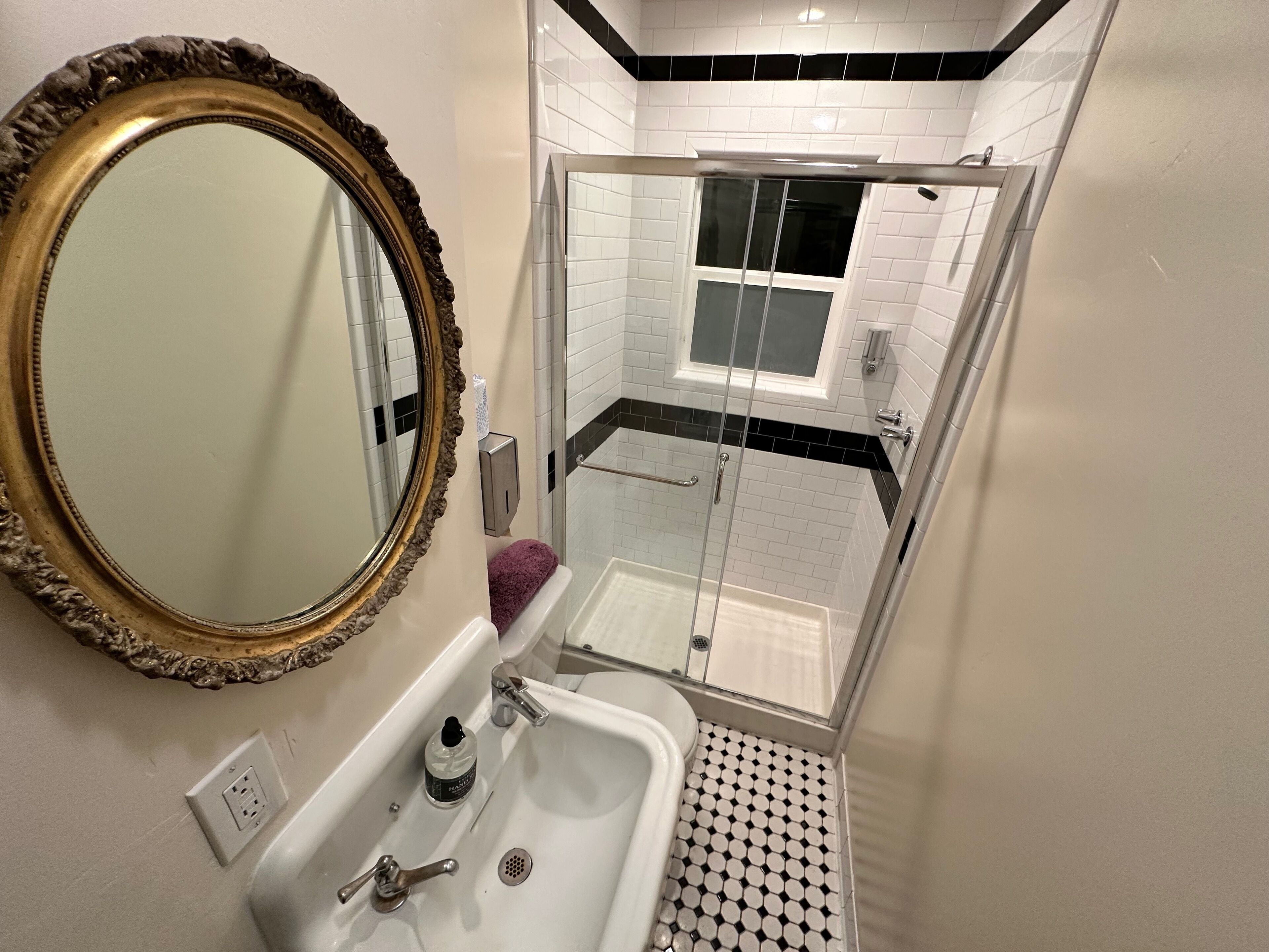 A bathroom with a large mirror, a sink, a handheld showerhead, and a glass-enclosed shower area.
