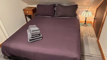 Een net opgemaakt bed met een paars sprei en een stapel handdoeken aan de linkerkant.