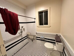 A compact bathroom with a white tiled floor and black and white geometric pattern, featuring a bathtub, toilet, and small shelf.