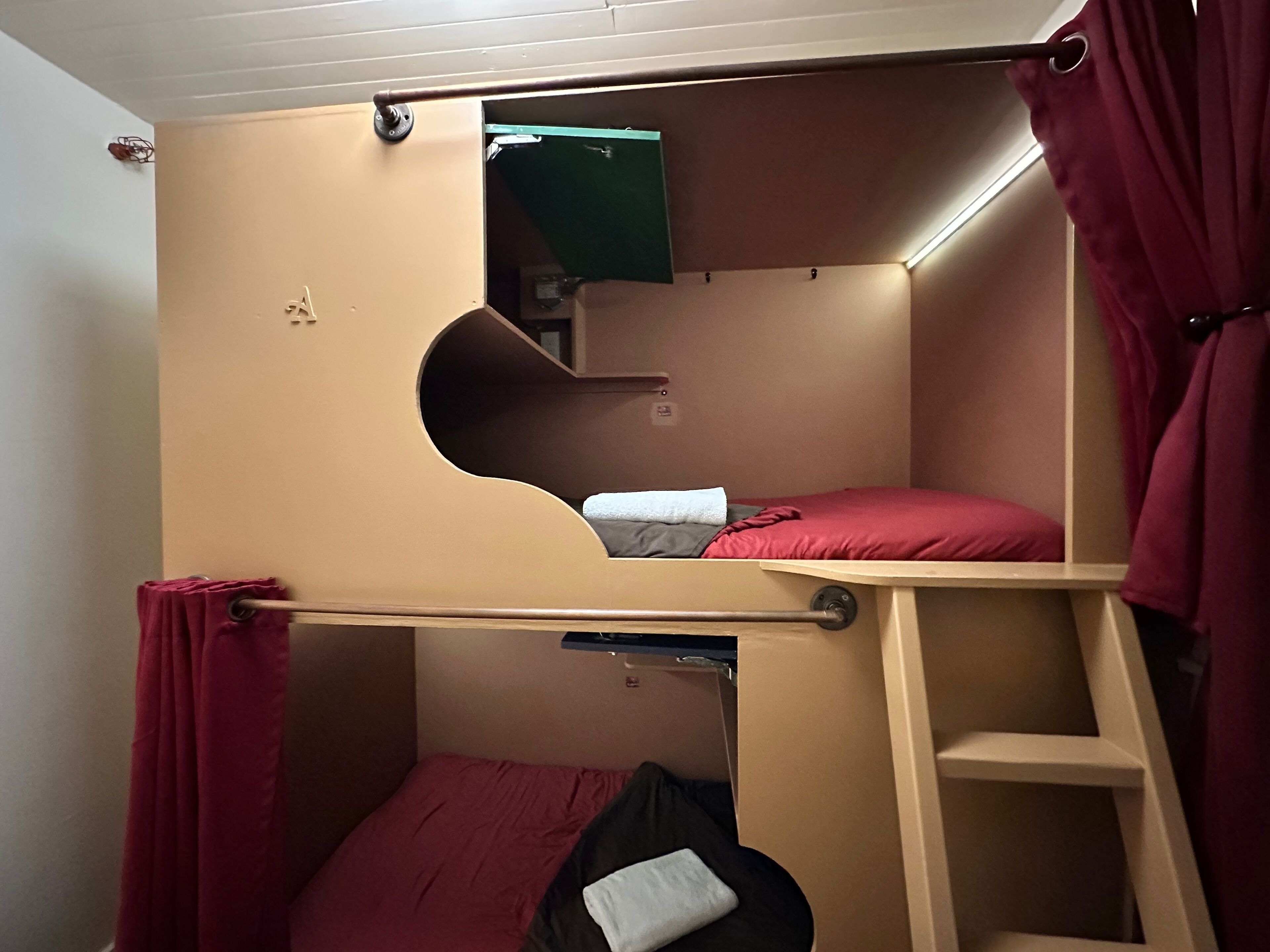 Een slaapkamer met een stapelbed, een ladder, een klein plankje en een spiegel.