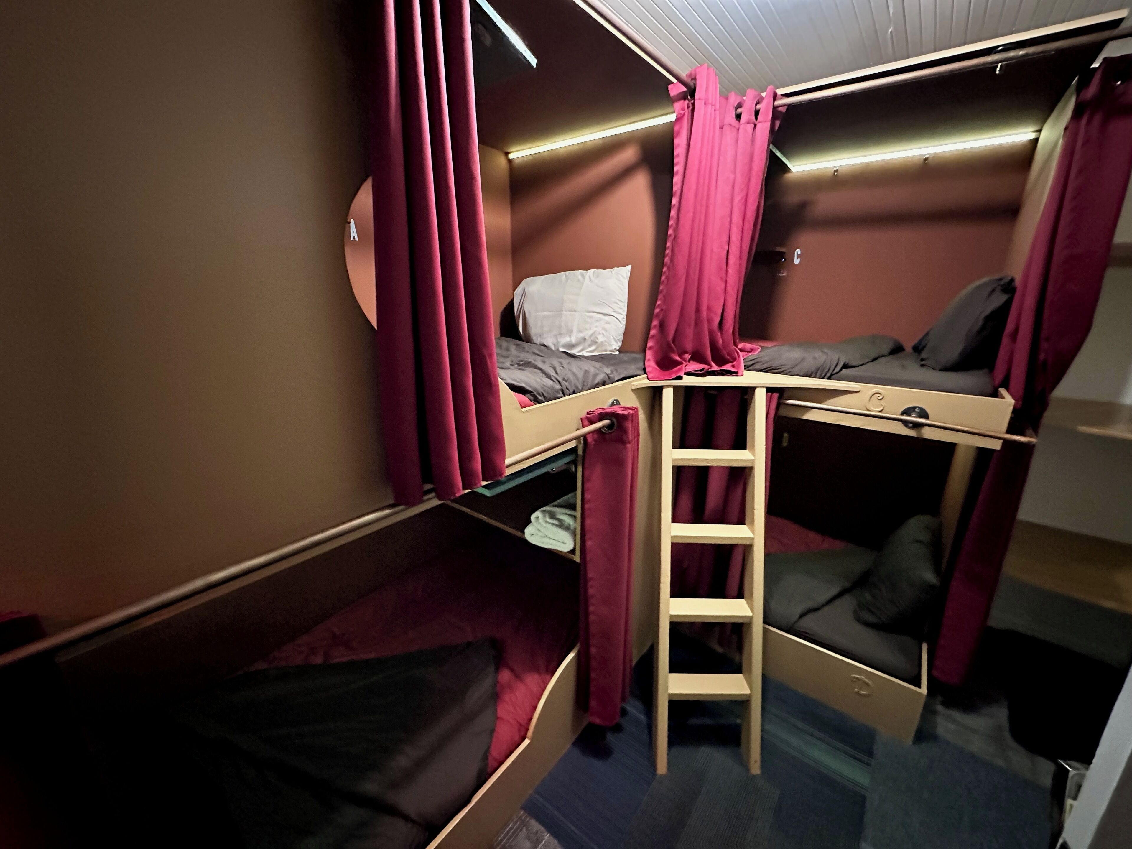 A compact, well-lit room with bunk beds, a ladder, and a small desk area.