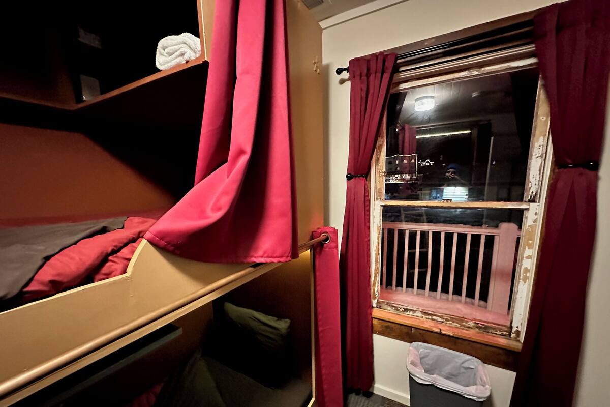 Une chambre avec un lit superposé, une fenêtre, des rideaux et une poubelle.