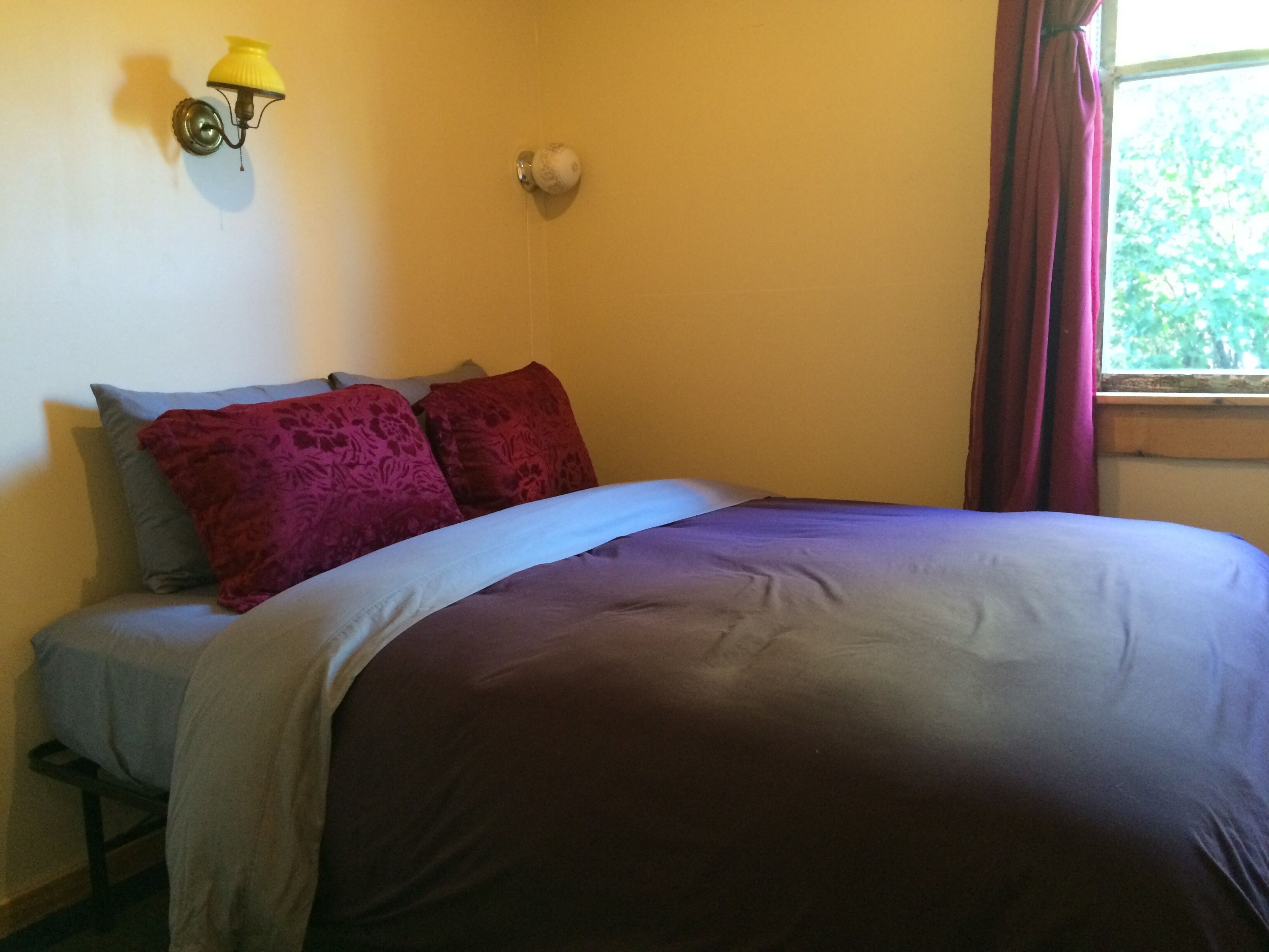 Una camera da letto con un letto, cuscini, una lampada a parete e una finestra con tende.